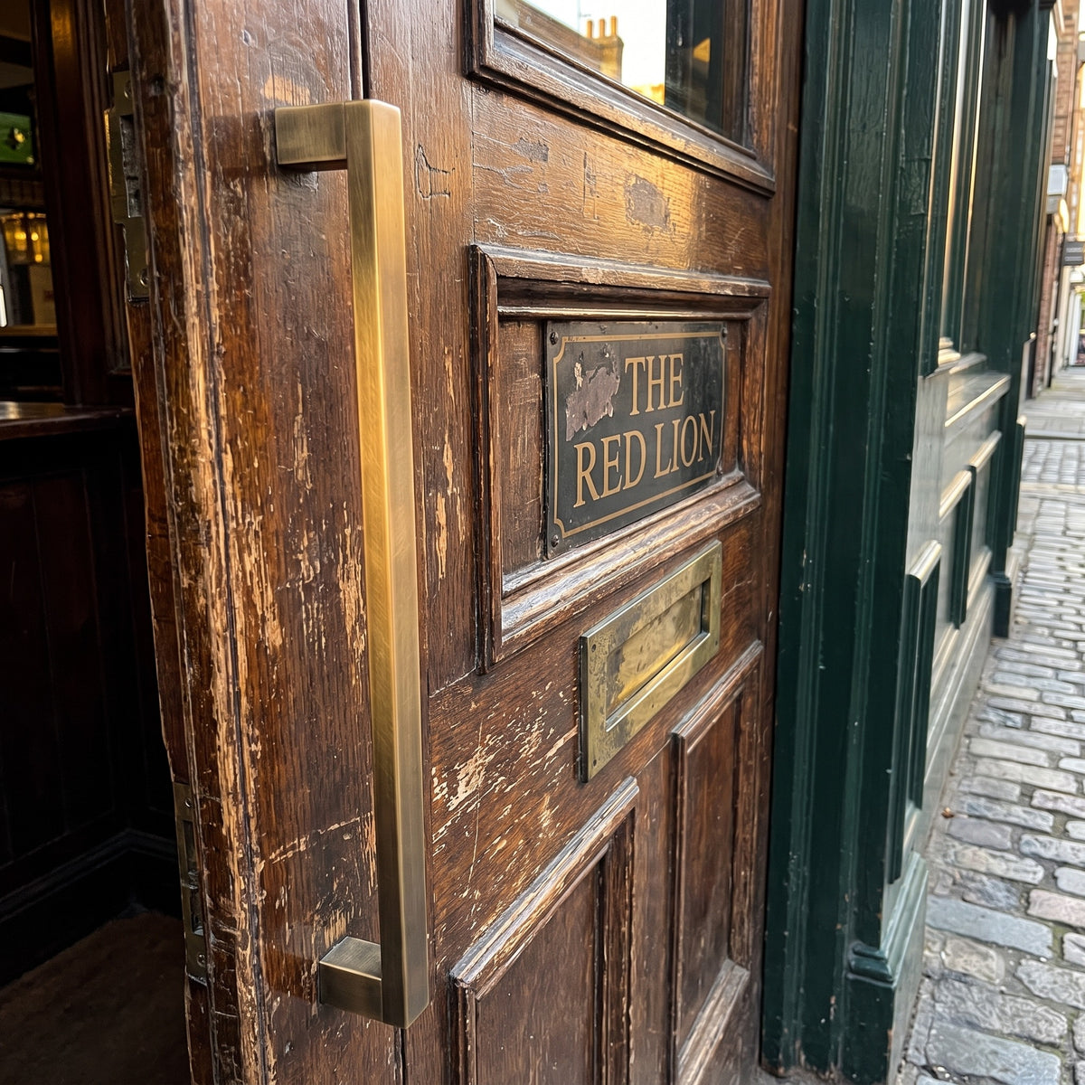 Digital render of the Bluff Bar Pull Handle in bronze, shown on a weathered timber entrance door