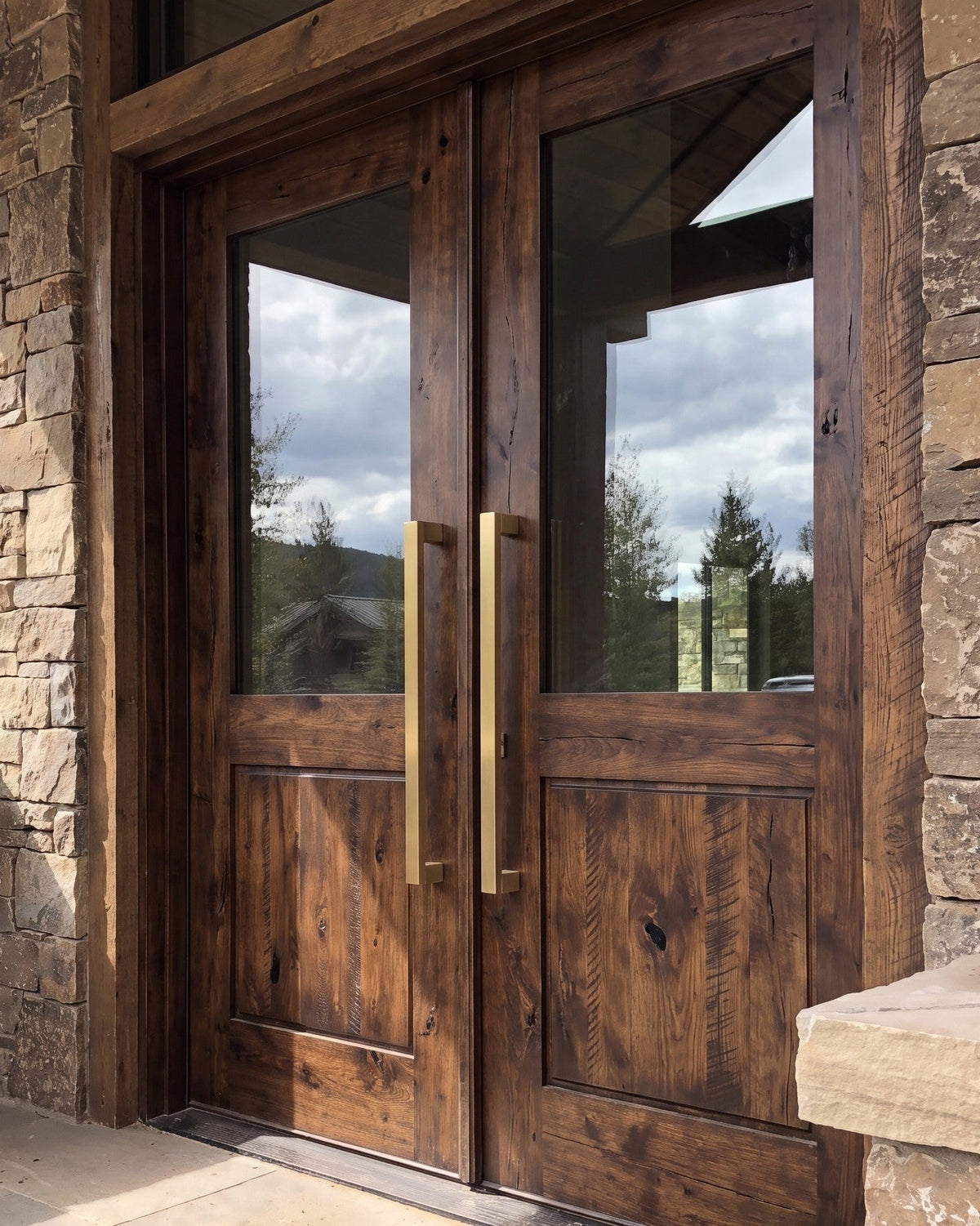 Bluff Bar pull handles in brass on rustic timber double entrance doors with a stone surround
